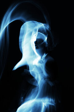 Abstract woman silhouette in light trails of light painting with blue light beams. Portrait in the style of light painting. Long exposure photo. Image contains noise and motion blur