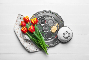 Composition with Passover Seder plate, kippah and flowers on light wooden background