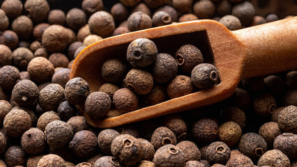 Wooden scoop full of allspice jamaica pepper close-up. Dried berries of the Pimenta dioica tree...