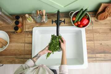 Woman washing greenery over ceramic sink in kitchen, closeup