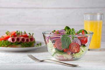 Sandwich with sausage and tomatoes, with salad and orange juice. European breakfast.