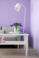 Vase with hyacinth flowers, Easter eggs and bunny on table in living room