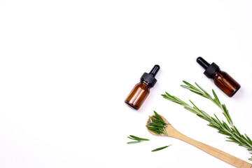 Aromatherapy herbal oil. Bottle glass with rosemary essential oil, wooden spoon, and fresh rosemary twig on white background.