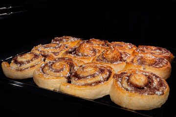 Twelve baked cinnamon buns on tray in electric oven. Swedish cuisine, homemade bakery, food, cooking and pastry concept