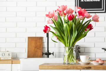 Beautiful tulips, cup and macarons on table in kitchen