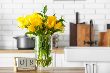 Vase with tulips and cube calendar with date 8 MARCH on table in kitchen. International Women's Day celebration