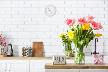 Beautiful tulips, gift box and cube calendar with date 8 MARCH on kitchen counter. International Women's Day celebration