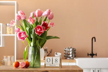 Vase with tulips, oranges and cube calendar with date 8 MARCH on table in kitchen. International Women's Day celebration