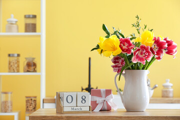 Jug with flowers, gift box and cube calendar with date 8 MARCH on kitchen counter. International Women's Day celebration