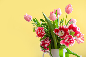 Jug with tulips on yellow background, closeup
