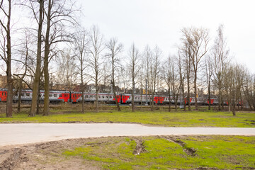 Electric train on railroad in suburbs behind bare trees, green grass, early spring