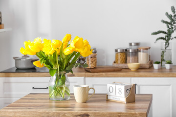 Vase with tulips, cup and cube calendar with date 8 MARCH on wooden table in light kitchen....