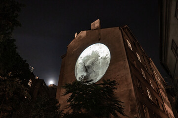 3d mapping of the moon on the wall of a building under a full moon at night.