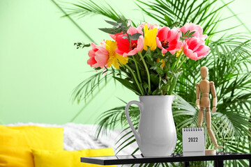 Vase with tulips, calendar and wooden mannequin on table in living room
