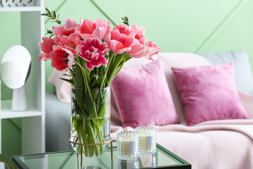 Vase with tulips and candles on table in living room