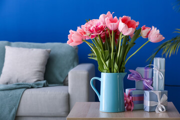 Vase with pink tulips and gift boxes on table in living room