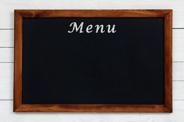 Black chalkboard with word Menu on white wooden background. Mockup for design