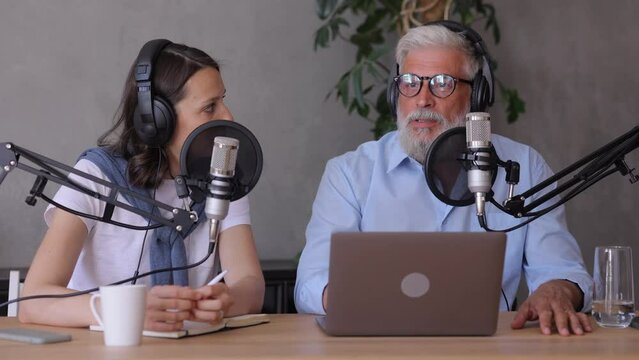 man and a woman record a podcast or interview with a microphone in a recording studio. an adult gray-haired man and a young European woman create audio content, record ads and audio books. adult