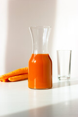 Composition with jug of fresh carrot juice, glass and vegetables (few carrots) on table, white background, vertical plane. It's low in calories, carbs while packing numerous nutrients, boosts immunity