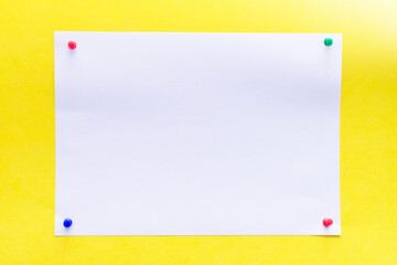 empty white sheet of paper pinned with push pins on a yellow background