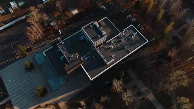 Contemporary flat roofed public building with large parking site at sunset in autumn aerial view. Cityscape and architecture