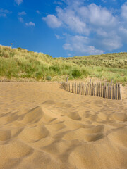 A sand dune with marram grass a the top and blue sky