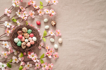 Fototapeta na wymiar Easter background with bird’s nest, colored easter eggs and blooming brunches on a beige background. Easter composition on a textured beige linen background. 
