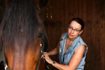 A woman harnesses her horse before riding.