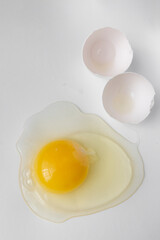 Broken egg with white and yolk spilled on the sides on white background