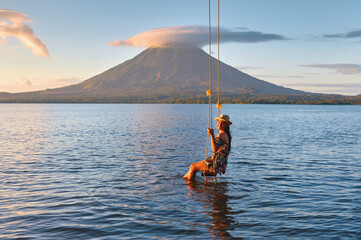 Woman sitting on swing in the lake with a beautiful view to the concepcion volcano during sunset in Ometepe island, Nicaragua