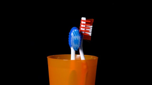 Two toothbrushes in an orange glass rotate on a black background 