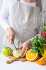 Young woman preparing homemade vitamin smoothie with apples, spinach, banana, kiwi, orange. Female hands. Process of preparation healthy food. Concept of clean eating, dieting, low calories food. 