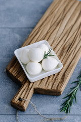 Soft Italian white cheese mozzarella on wooden board in white bowl served with fresh rosemary branch