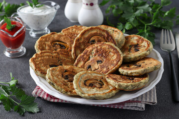 Fried fritters with champignons, garlic and parsley, served for breakfast with sour cream and tomato ketchup on dark background