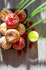 beautiful bright donuts on a gray wooden background surrounded by raspberries and corn flakes with glasses of exotic juices