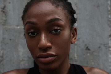 Close-up of confident afro woman with black braided hair posing on dark wall.