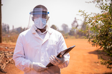 Portrait of a successful African doctor, he wears a lab coat, a surgical mask and a protective face...