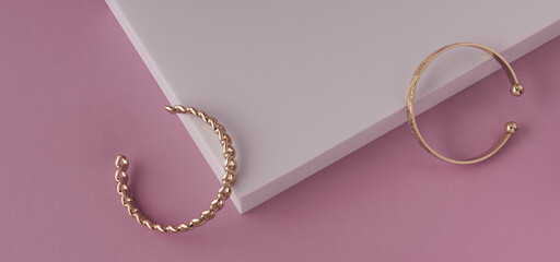 Panorama of two modern gold chain shape bracelet and modern cuff on white and pink background