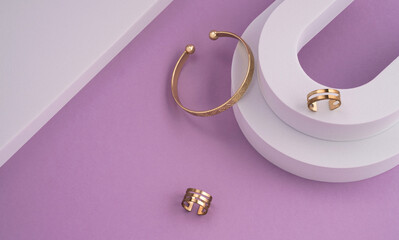 Top view of geometric flat lay of modern golden bracelet and rings on white and purple background with copy space