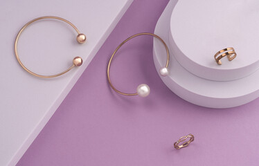 Top view of modern golden bracelets and rings on white podium on pink background with copy space