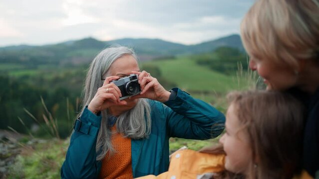 Senior woman taking picture of her daughter and granddaughter on top of mountain.