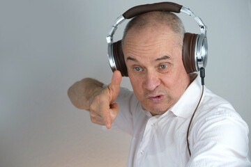 close-up of mature charismatic man 60 years in headphones listening to music with emotions on face...