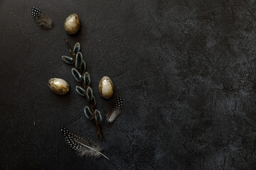 Happy Easter concept. Preparation for holiday. Golden decorated easter eggs willow feather on trendy grunge scratched dark black shale background. Simple minimalism flat lay top view copy space