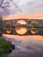 Roman bridge of Ourense reflected in the Miño river in a beautiful sunset.