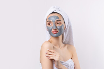 A woman with a gray clay cosmetic mask in a white towel on her head on a white background.