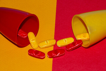 red small glass cup with red pills on a yellow background that go into a yellow small cup that has yellow pills and is on a red background creative concept of pill exchange