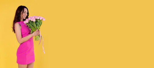 Beautiful girl with a bouquet of pink tulips. Smiling young woman with flowers on a yellow background. Banner