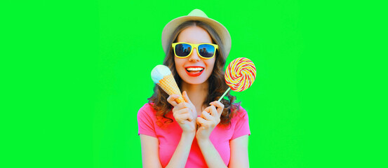 Portrait of happy laughing young woman with ice cream and lollipop wearing summer straw hat on green background