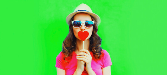 Portrait of young woman with red heart shaped lollipop on green background