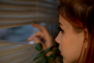Teenage girl look out the window through the blinds